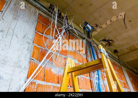 Échelles pour faciliter l'installation des câbles, boîtes de distribution pour l'électricité. Un tas de câbles sont suspendus du plafond, passant entre les planchers i Banque D'Images