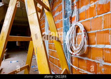 Échelles pour faciliter l'installation des câbles, boîtes de distribution pour l'électricité. Un tas de câbles sont suspendus du plafond, passant entre les planchers i Banque D'Images