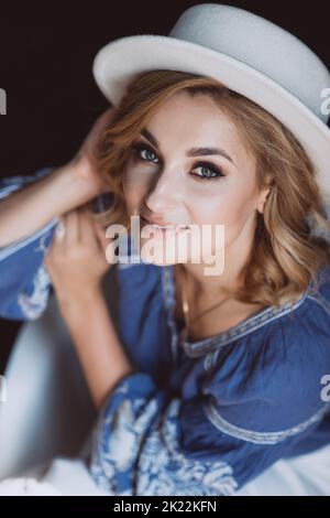 Beautiful stylish elegant blonde woman in ethnic clothes in an embroidered shirt in a white hat in the interior in grunge style. Ukrainian national cl Stock Photo