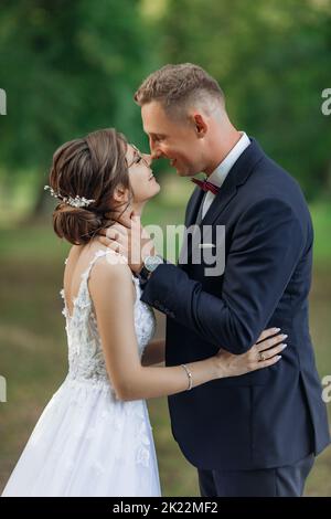 Jeune homme marié mettant les bras autour du cou de jeune femme mariée, embrassant, rencontrant les yeux, embrassant. Célébration. Banque D'Images