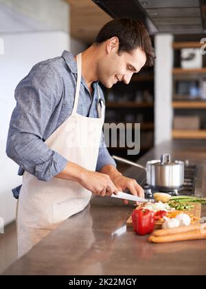 Les vrais hommes cuisinent. Un beau jeune homme qui hache des légumes dans sa cuisine Banque D'Images