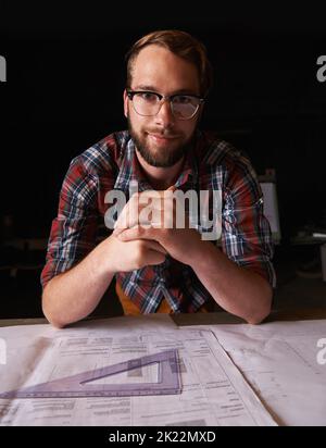 Laissez la beauté que nous aimons devenir ce que nous faisons. Un jeune homme assis à l'intérieur travaillant sur des plans de construction. Banque D'Images