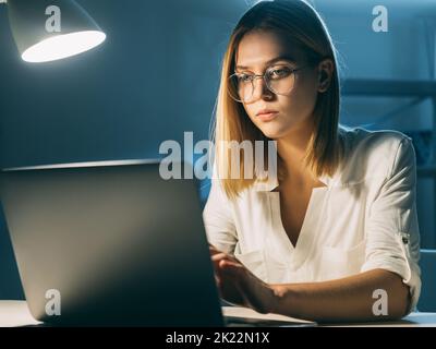 Travail à distance. Nouveau style de vie normal. Consultant commercial indépendant. Femme intelligente qui tape tard dans la nuit sur un ordinateur portable dans un espace de travail Banque D'Images