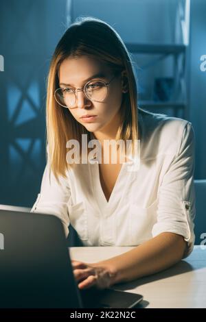 Travail à distance. Mode de vie en cas de pandémie. Travailler à domicile. Femme concentrée travaillant sur la saisie d'un ordinateur portable dans un espace de travail sombre Banque D'Images