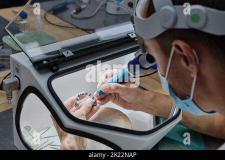 Dentiste moulins à main couronnes de dent créées sur 3D imprimante pour métal. Technicien dentaire travaillant avec des couronnes en céramique dans une boîte de protection au laboratoire. Banque D'Images