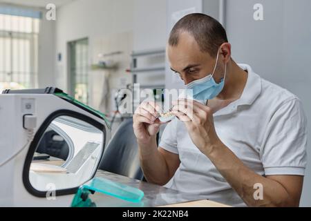 Dentiste moulins à main couronnes de dent créées sur 3D imprimante pour métal. Technicien dentaire travaillant avec des couronnes en céramique dans une boîte de protection au laboratoire. Banque D'Images