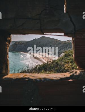 Un plan vertical de la magnifique rive de la mer avec la falaise vue à travers un trou dans un mur de pierre Banque D'Images