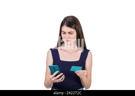 Perplexed young woman looks confused at her smartphone while holding a credit card in other hand, isolated on white background with copy space. Intern Stock Photo