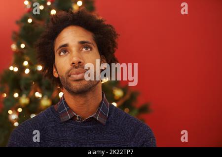 C'est l'heure de Noël. Un beau jeune homme debout devant un arbre de Noël qui a l'air bien pensé Banque D'Images