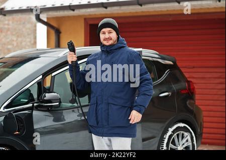 Un jeune homme charge sa voiture électrique en hiver.Concept de transport écologique. Banque D'Images