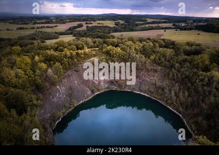 Petit lac bleu cratère d'un volcan dormant entouré de forêt aux couleurs de l'automne et de montagnes à l'horizon, en Allemagne Banque D'Images