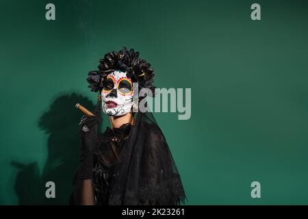 Femme dans le jour de la mort costume d'halloween tenant le cigare sur fond vert, image de stock Banque D'Images