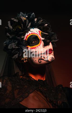 Portrait d'une femme en fête mexicaine de costume mort debout sur fond bordeaux, image de stock Banque D'Images