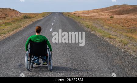 Woman in a wheelchair on a highway in the steppes.  Stock Photo