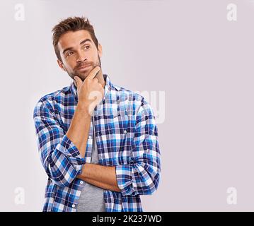 Considérant toutes les options. Un beau jeune homme dans la pensée profonde sur un fond gris. Banque D'Images