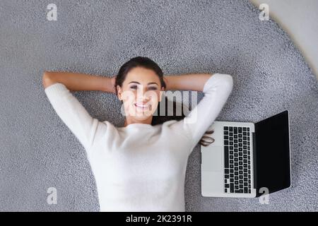 Si facile il fonctionne presque lui-même. Une jeune femme couché sur un tapis à côté d'un ordinateur portable Banque D'Images