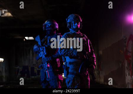 Les soldats de la guerre moderne dans l'obscurité avec des munitions de combat et des armes dans les mains de lasers équipés sont en ordre de bataille. Supports mixtes. Banque D'Images