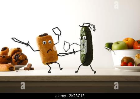 Healthy eating and unhealthy food concept with cucumber battling chocolate muffin on kitchen bench with isolated background. Front view. Stock Photo