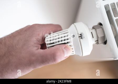 vue rapprochée de la personne qui abaisse le thermostat du radiateur à zéro pour économiser de l'énergie et de l'argent, augmenter les coûts d'énergie et de chauffage concept Banque D'Images