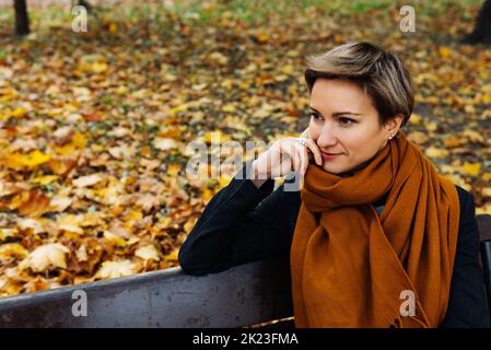 Portrait d'une blonde aux cheveux courts dans un foulard en terre cuite dans un parc d'automne Banque D'Images