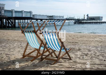 Deux chaises longues bleues et blanches sur une plage de sable avec jetée de Sandown en arrière-plan. Vue traditionnelle britannique sur le bord de mer. Banque D'Images