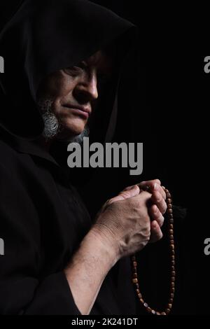 moine médiéval dans la calotte tenant le rosaire isolé sur noir, image de stock Banque D'Images