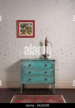Mur de briques blanches avec théière en cuivre antique sur le dessus de l'élégant cabinet turquoise vintage et peinture pendu dans le salon Banque D'Images