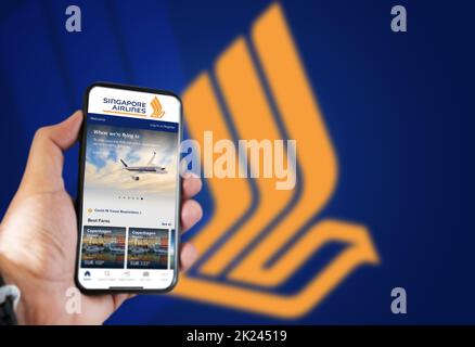 Singapour, octobre 2021 : main tenant un téléphone avec l'application de réservation de vols Singapore Airlines.Logo Singapore Airlines flou sur fond bleu Banque D'Images