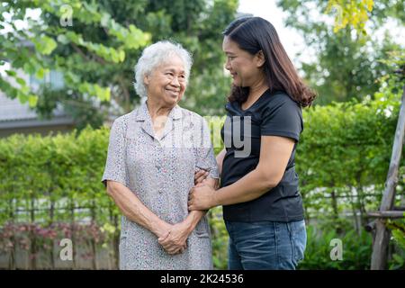 Femme asiatique âgée avec un aidant plus jeune marche et accolade avec heureux dans le parc naturel. Banque D'Images