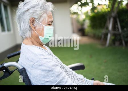 Femme asiatique âgée ou âgée en fauteuil roulant et portant un masque facial pour protéger l'infection à Covid-19 coronavirus dans le parc. Banque D'Images