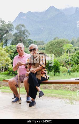 Vertical of asian senior couple sit on a bench on vacation outdoors. Stock Photo