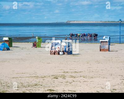 Plage ensoleillée avec chaises de plage sur la plage de sable au premier plan et un groupe guidé au début d'une randonnée à la boue et une vue sur l'île de Banque D'Images