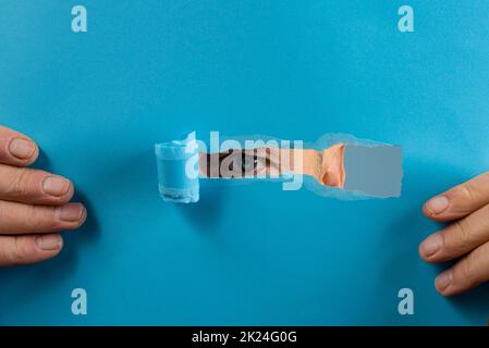 l'œil d'un homme regardant à travers la déchirure dans une feuille de papier Banque D'Images