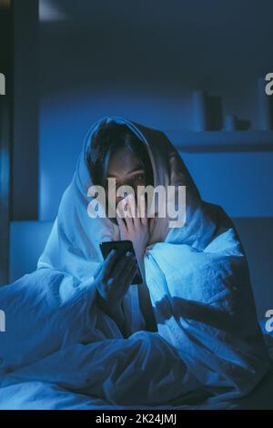 Night insomnia. Late online. Stress anxiety. Social media addiction. Terrified scared girl reading disturbing Internet news on mobile phone sitting on Stock Photo