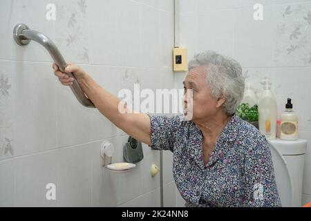 Asiatique senior ou âgée vieille femme patiente utilisation de la pente passerelle de la poignée de sécurité avec aide assistant de soutien dans la salle de soins infirmiers d'hôpital; sain fort Banque D'Images