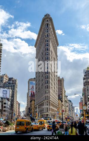 Vue à angle bas du bâtiment Flatiron avec beaucoup de taxis jaunes passant par et des gens devant pendant la journée ensoleillée d'hiver, ciel nuageux en arrière-plan, ve Banque D'Images