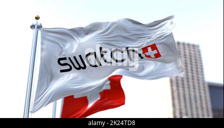 Berne, CH, mars 2022: Le drapeau avec le logo Swatch agitant dans le vent avec le drapeau national de la Suisse flou en arrière-plan. Swatch est un SW Banque D'Images