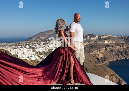 Imerovigli, Santorini, Grèce - 29 juin 2021: Femme en robe rouge et homme athlétique lors d'une séance photo romantique à Imergovigli sur l'île de Santorini Banque D'Images