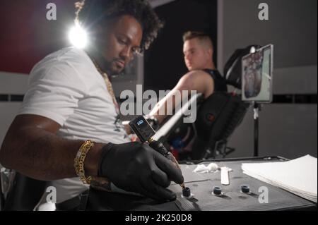 L'artiste professionnel américain de tatouage d'Afrique fait un tatouage sur le bras de client. Photographie de haute qualité. Banque D'Images