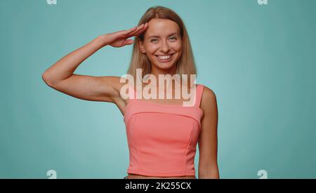 Oui, monsieur. Femme blonde subordonnée, responsable, sérieuse saluant écouter l'ordre comme si soldat, suivant la discipline, obéissant exprimant la confiance. Jeune jolie fille sur fond de studio bleu Banque D'Images