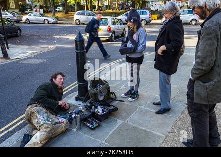 Artist Ben Wilson, who creates tiny paintings on chewing gum on the pavement, discusses his work with onlookers, North London, UK Stock Photo