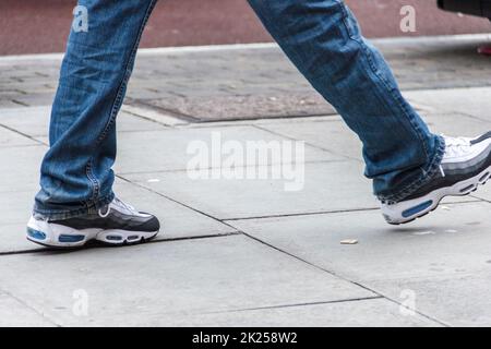 Low-angle view of a person wearing trainers walking along the road, London, UK Stock Photo