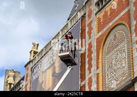 Amsterdam, Netherlands - August 2022: People standing on a cherry picker platform fixing a large banner to the outside wall of the famous Rijks Museum Stock Photo