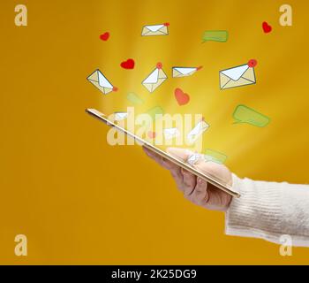 la main femelle tient une tablette avec des coeurs, des dialogues et des lettres volant sur un fond jaune. Dépendance aux médias sociaux, réception de correspondance et évaluation. Multitâche Banque D'Images