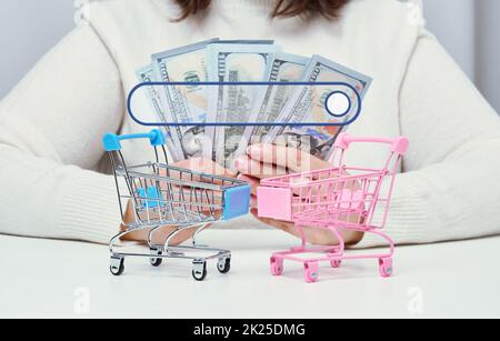 Une femme tient des dollars de papier américain dans ses mains et deux mini-chariots de magasinage sur la table. Le concept du début des ventes dans les magasins en ligne, la recherche d'une offre rentable Banque D'Images