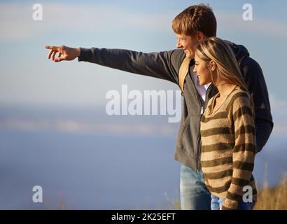 C'est un beau jeune homme qui pointe sur quelque chose que sa copine peut voir pendant une randonnée Banque D'Images