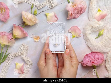 Femme mains tenant une boîte cadeau avec un anneau de perle avec des fleurs rose clair autour Banque D'Images