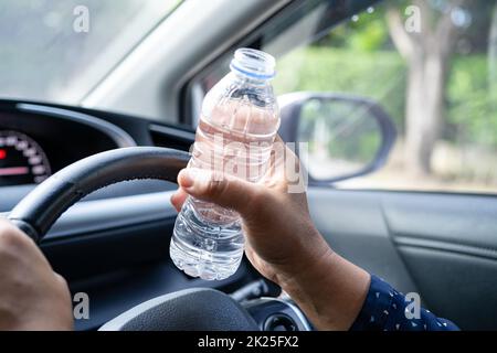 Femme asiatique chauffeur tenant une bouteille pour boire de l'eau tout en conduisant une voiture.Une bouteille d'eau chaude en plastique peut provoquer un incendie. Banque D'Images