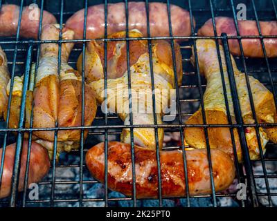 Des cuisses de poulet et des saucisses de viande sur une grille de fer. Banque D'Images