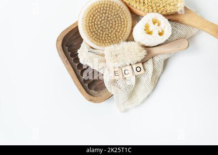 Zéro déchet, salle de bain durable et style de vie. Pinceau de bambou, éponge de loofah, pinceau de massage de cactus sur fond blanc. L'inscription Eko en lettres de bois. Banque D'Images